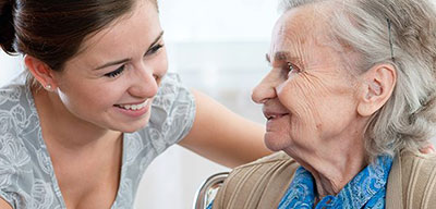 young female caregiver and elderly woman talking and smiling